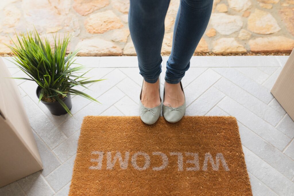 Low section of Caucasian woman standing near welcome mat in front of door at home
